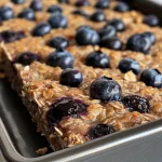 An appetizing close-up image of Blueberry Baked Oatmeal, highlighting the oats and juicy blueberries.
