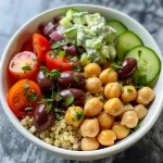 Juicy Mediterranean chickpea bowl featuring chickpeas, chopped vegetables, and a drizzle of tzatziki on top.