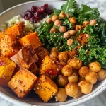 A hearty bowl filled with chickpeas, sweet potatoes, pepitas, and cranberries.