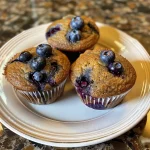 Delicious blueberry protein muffins displayed with fresh blueberries in the background.