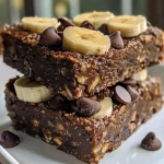 Side view of a moist Chocolate Banana Oatmeal Breakfast Bar displayed on a wooden cutting board.