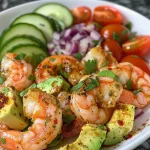 An appetizing arrangement of shrimp and avocado mixed with fresh vegetables and herbs in a bowl.