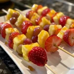 Side view of vibrant fruit kabobs, including red strawberries, yellow pineapple, green grapes, and banana, with honey yogurt.