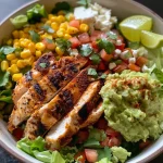 An appetizing chicken taco bowl showcasing ingredients like grilled chicken, guacamole, and lime on a bed of lettuce.