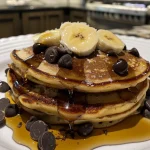 A close-up view of fluffy banana chocolate chip pancakes stacked on a plate.