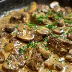 Juicy beef cubes and mushrooms in a creamy sauce served in a skillet.