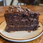 A close-up side view of a moist chocolate cake with rich frosting and chocolate chips.