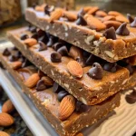 ['A close-up side view of vegan almond butter protein bars, showing layers and chocolate chips.', 'Juicy almond butter protein bars with chocolate chips, displayed from a side angle.', 'Delicious almond butter protein bars, highlighting their texture and ingredients from a close-up view.', 'An iPhone photo of vegan almond butter protein bars, featuring a side perspective with visible chocolate chips.']