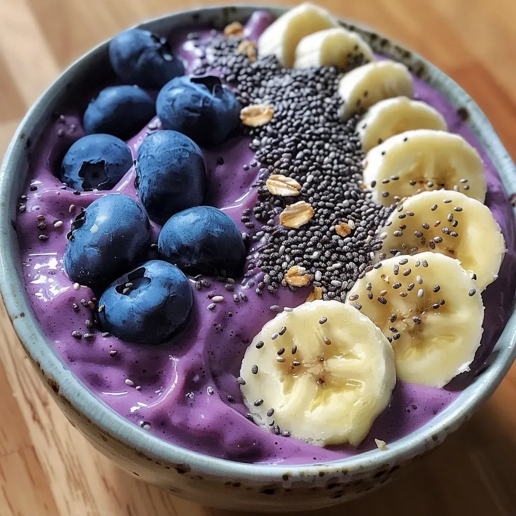 ['Close-up view of a Blueberry Banana Smoothie Bowl topped with fresh blueberries and chia seeds.', 'Side view of a vibrant Blueberry Banana Smoothie Bowl with a creamy texture and colorful toppings.', 'Detailed shot of a Blueberry Banana Smoothie Bowl showcasing frozen bananas, blueberries, and chia seeds.', 'A delicious Blueberry Banana Smoothie Bowl filled with rich colors and garnished with nuts and seeds.']
