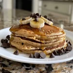Close-up view of a stack of chocolate chip banana protein pancakes topped with chocolate chips.