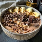['Close-up view of a Chocolate Coconut Protein Smoothie Bowl topped with granola and fresh fruit.', 'Side angle of a smoothie bowl featuring chocolate and coconut, garnished with cacao nibs and yogurt.', 'Delicious Chocolate Coconut Protein Smoothie Bowl in a bowl, decorated with coconut flakes and chocolate chips.', 'Vibrant Chocolate Coconut Protein Smoothie Bowl showcasing a blend of toppings including granola and fresh fruit.']