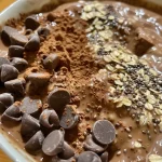 ['A close-up side view of a bowl of chocolate protein overnight oats topped with mini chocolate chips.', 'Side view photo of creamy chocolate oats in a glass jar, garnished with chocolate chips.', 'Close-up image of overnight oats with a rich chocolate hue, featuring chocolate chips and chia seeds.', 'A detailed shot of chocolate protein overnight oats displaying a smooth texture and toppings.']