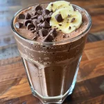 Close-up view of a creamy chocolate smoothie in a glass, featuring visible layers and a garnish.