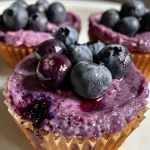 ['Close-up of blueberry protein cups with a creamy texture and fresh blueberries on top.', 'Side view of delicious blueberry protein cups in a white dish, showcasing their vibrant color.', 'Juicy blueberry protein cups filled with blueberries and cottage cheese, captured with a smartphone.', 'Tasty blueberry protein cups arranged neatly, highlighting their rich purple hue and creamy filling.']