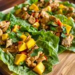 ['Close-up of Chicken Mango Lettuce Wraps with vibrant ingredients including diced mango and red bell pepper.', 'Juicy Chicken Mango Lettuce Wraps arranged on a plate, showcasing fresh herbs and crisp lettuce.', 'Side view of a delicious Chicken Mango Lettuce Wrap, highlighting the colorful filling and lettuce cup.', 'Freshly made Chicken Mango Lettuce Wraps filled with chicken, mango, and vegetables, ready to eat.']