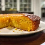 ['Close-up side view of a slice of moist mango cake topped with mango slices.', 'Side view of a delicious mango cake with vibrant yellow mango puree on top.', 'Juicy mango cake slice with a rich texture and colorful fruit garnish.', 'Luscious mango cake with a golden hue, featuring a smooth frosting and fresh mango.']