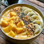 ['Close-up view of a vibrant mango smoothie bowl topped with colorful fruit.', 'A side view of a creamy mango smoothie bowl filled with tropical fruits and nuts.', 'Juicy mango smoothie bowl with a smooth texture and garnished with sliced fruits.', 'Bright mango smoothie bowl displaying a rich yellow color and fresh toppings.']
